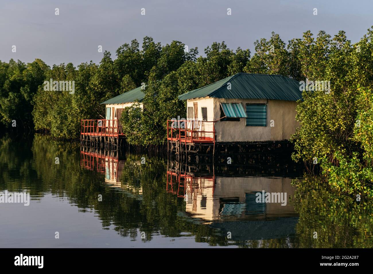 Holzhaus mit und Veranda umgeben von Bäumen durch glattes Meer über blauem Himmel Stockfoto