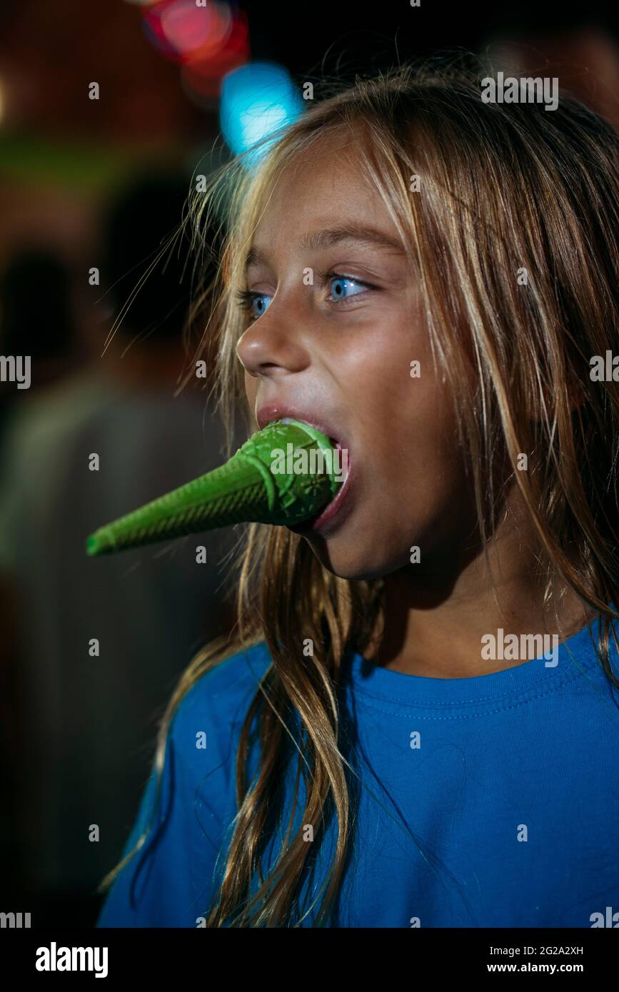 Kleines blondes Mädchen, das nachts im Vergnügungspark ein leckeres Eis isst Stockfoto