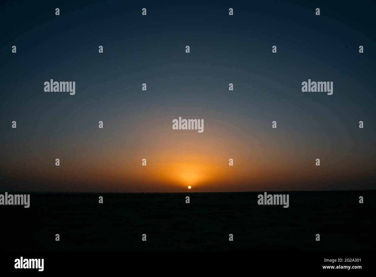 Herrlicher Blick auf den wolkenlosen Abendhimmel mit untergehenden Sonnenstrahlen über dem trockenen Sand der majestätischen Sahara-Wüste Stockfoto