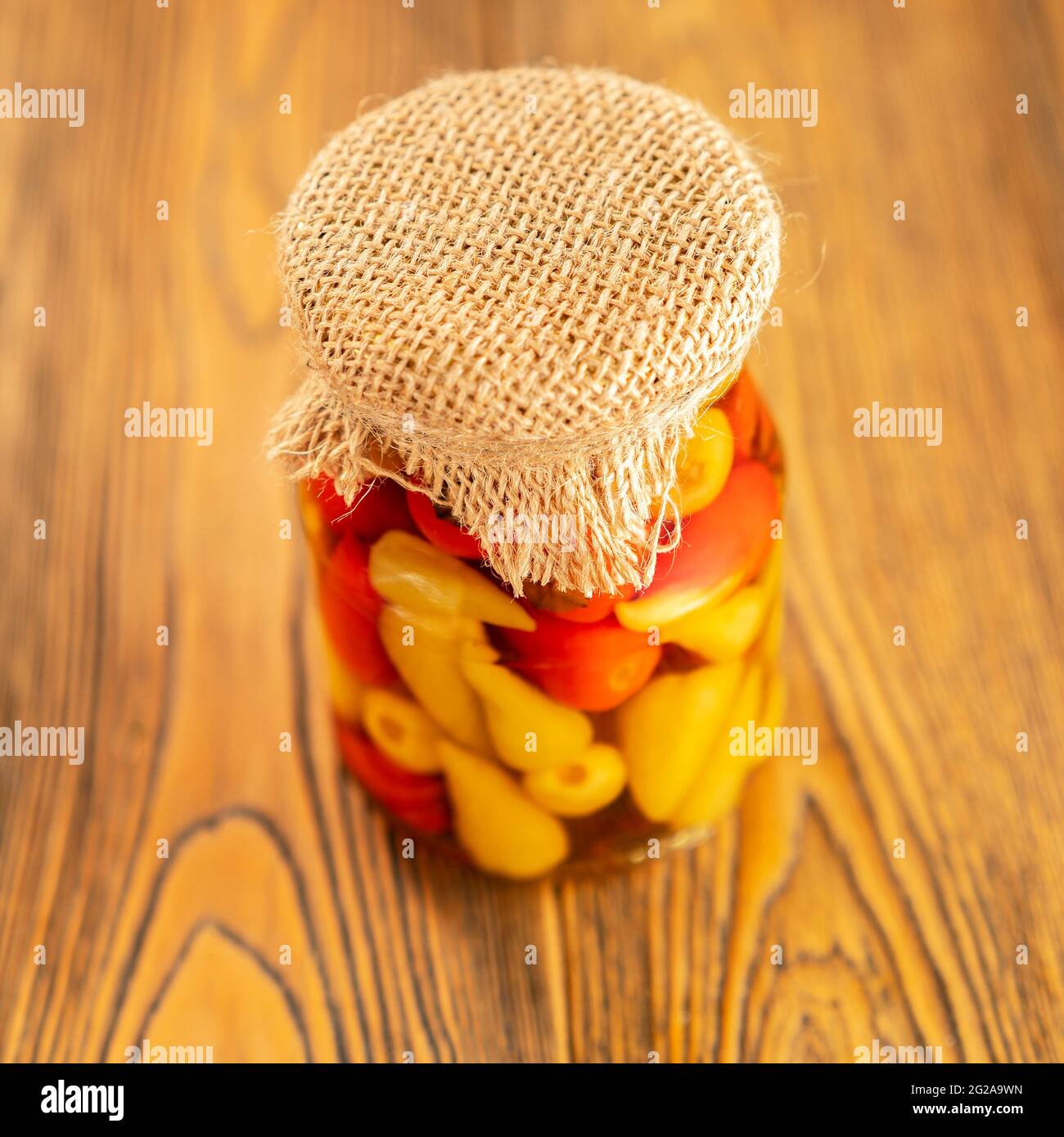 Eingelegter Pfeffer in einem Glas. Hausgemachte Zubereitungen auf rustikale Weise. Ein würziger Snack. Gebunden mit Jute-Faden. Rustikaler Stil. Selektiver Fokus. Stockfoto