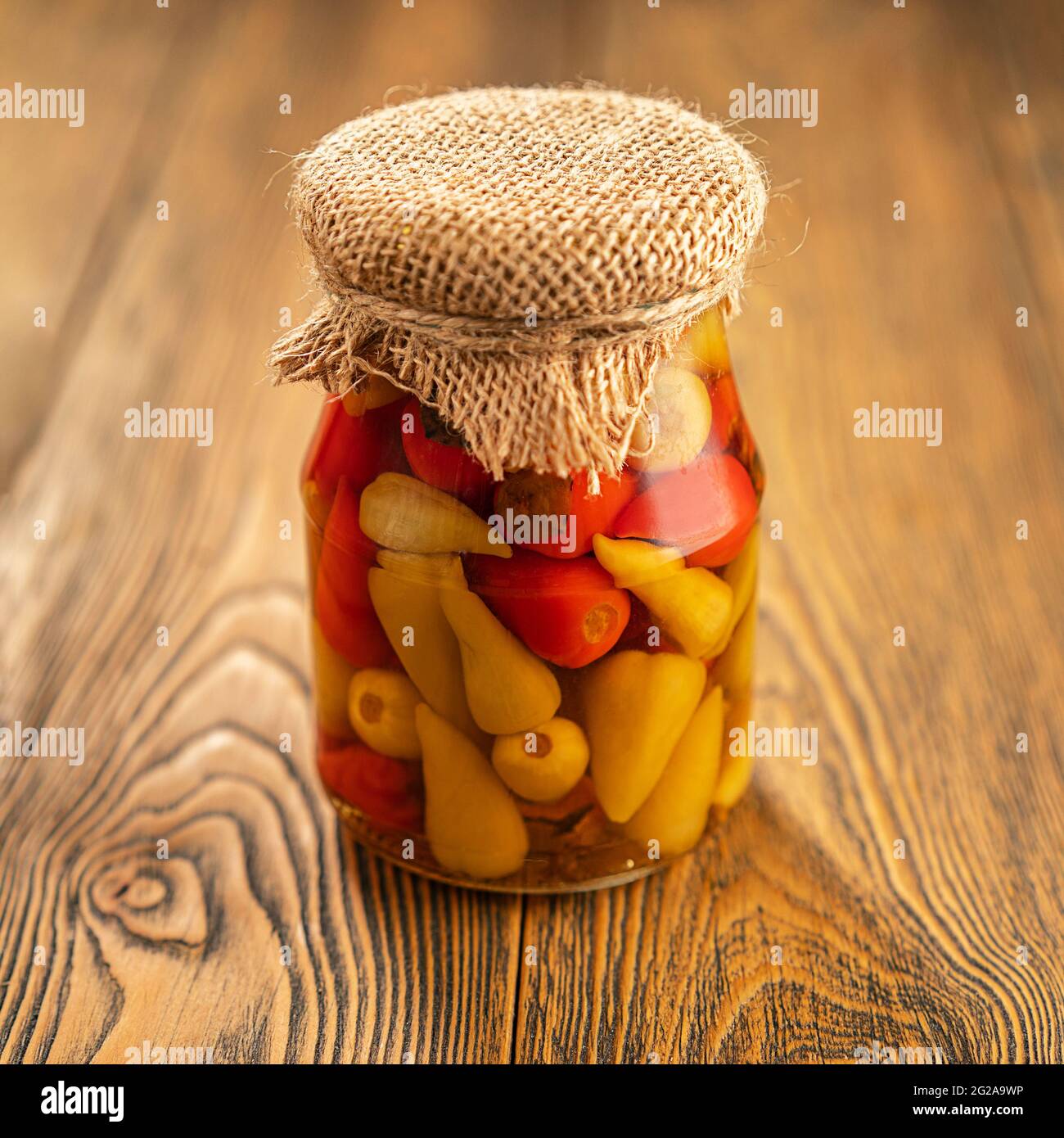 Eingelegter Pfeffer in einem Glas. Hausgemachte Zubereitungen auf rustikale Weise. Ein würziger Snack. Gebunden mit Jute-Faden. Rustikaler Stil. Selektiver Fokus. Stockfoto