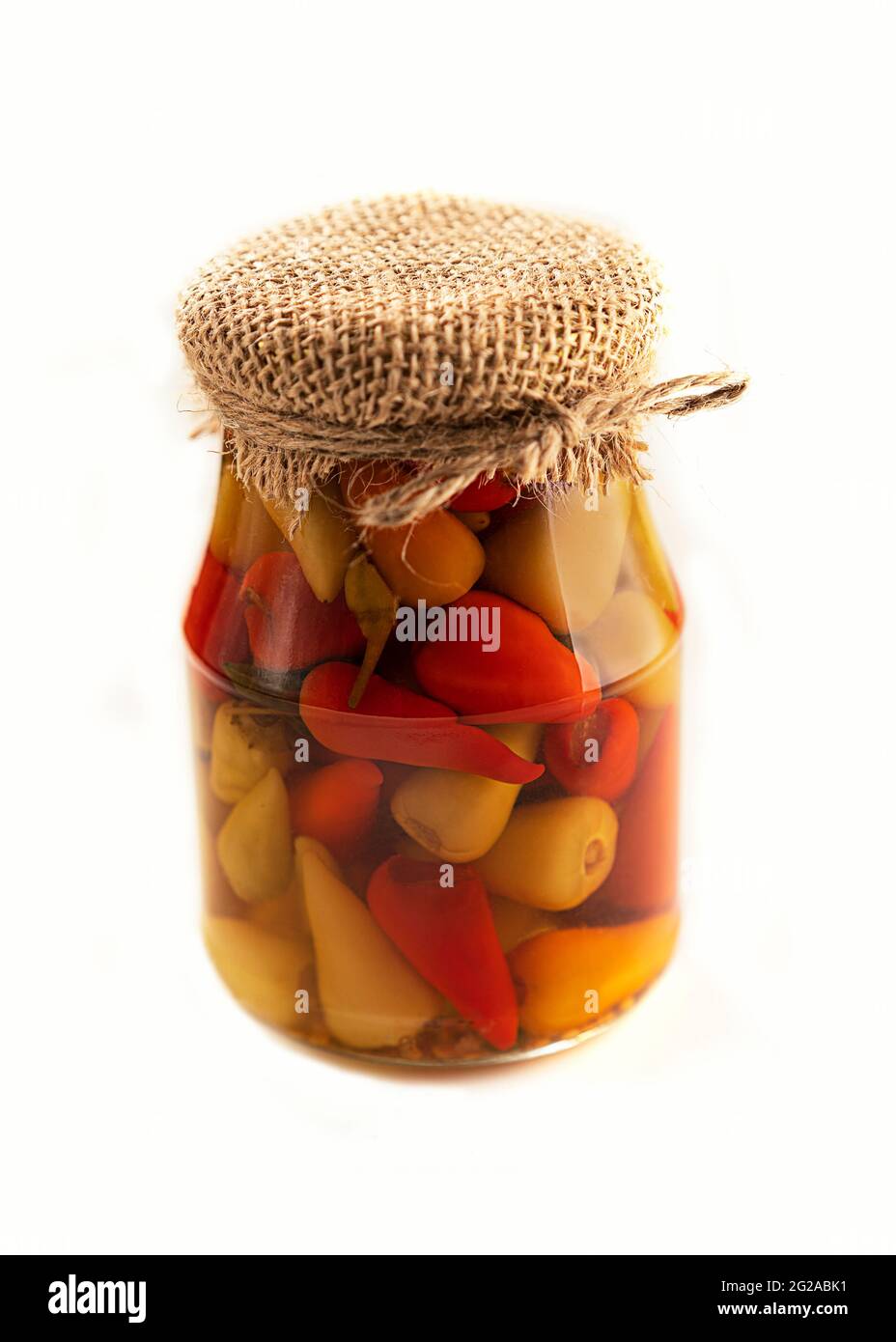 Eingelegter Pfeffer in einem Glas. Isoliert auf weißem Hintergrund. Ein würziger Snack. Gebunden mit Jute-Faden. Rustikaler Stil. Selektiver Fokus. Stockfoto