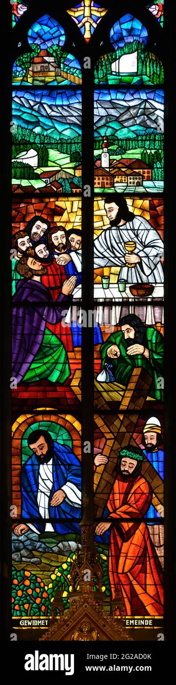 Buntglasfenster mit Darstellung des Letzten Abendmahls und Jesu mit dem Kreuz. Oben befindet sich die Stadt Erl in Tirol mit ihrer Kirche. Votivkirche. Stockfoto