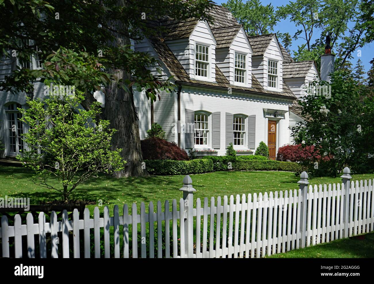 Haus mit Dachfenstern und weißem Zaun umgeben von Bäumen Stockfoto