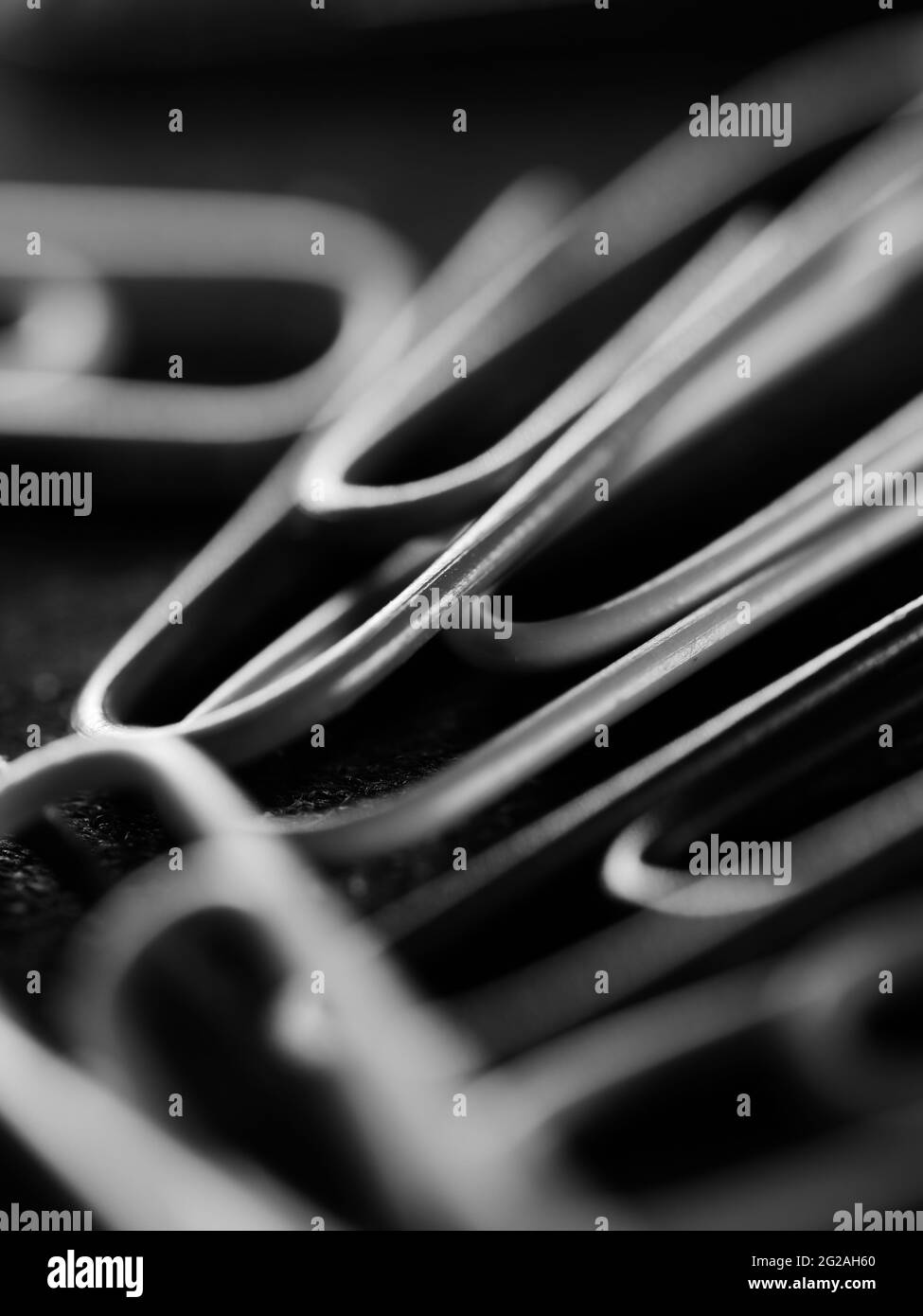 Vertikale Graustufenaufnahme von verstreuten Büroklammern auf einer schwarzen Oberfläche Stockfoto