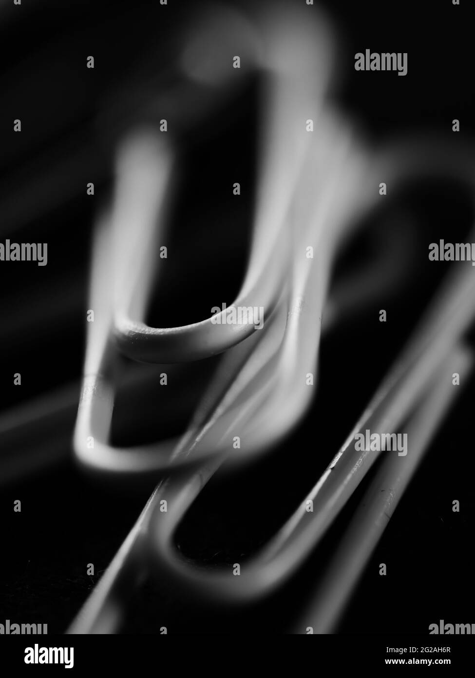 Vertikale Graustufenaufnahme von Büroklammern auf einem unscharfen schwarzen Hintergrund Stockfoto
