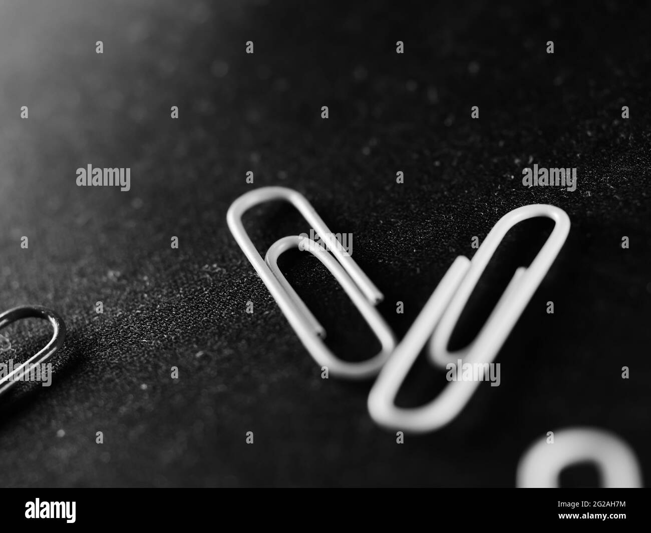 Selektive Graustufenaufnahme von zwei verstreuten Büroklammern mit Licht aus der Ecke Stockfoto