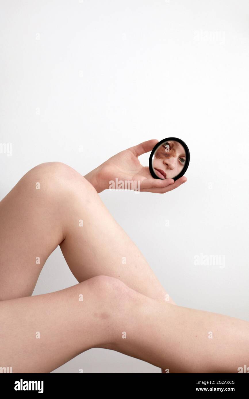 Schneiden Sie junge Frau mit nevus Geburtsmarke unter dem Auge reflektiert in kleinen runden Spiegel, während Blick auf die Kamera auf weißem Hintergrund Stockfoto