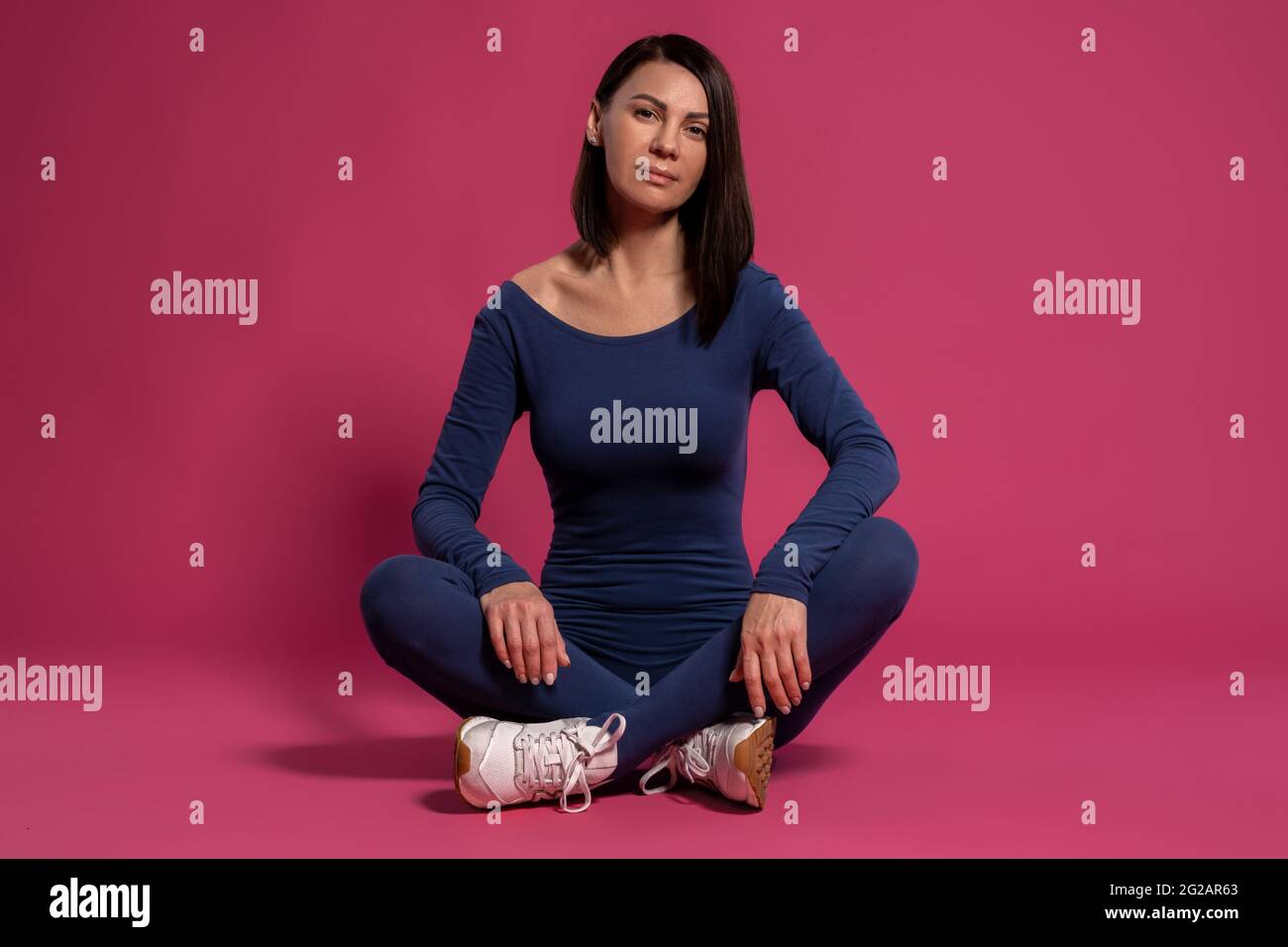 Ruhige Frau im Fitness-Jumpsuit, die mit gekreuzten Beinen auf dem Boden sitzt Stockfoto