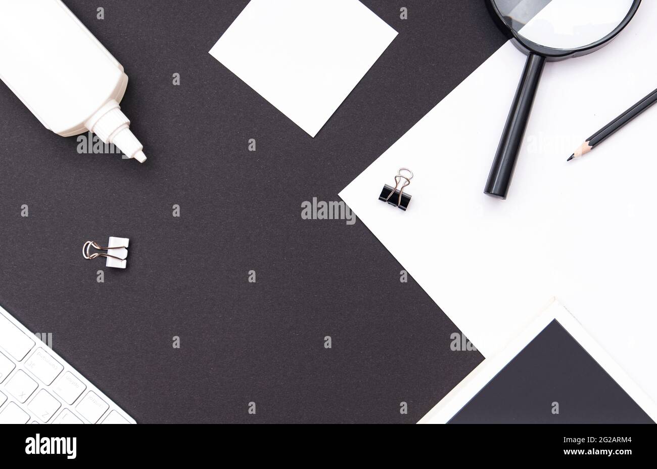Modell am Arbeitsplatz in kontrastierenden Schwarz- und Weißtönen. Schreibtisch mit Schreibwaren, Buch, leerem Blatt, Lupe, Tastatur und Bleistift. Draufsicht, Platz fo Stockfoto