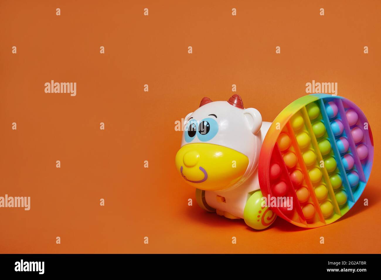 Anti-Stress-Spielzeug Pop it und Spielzeug Kuh auf orangefarbenem Hintergrund mit Kopieplatz. Stockfoto