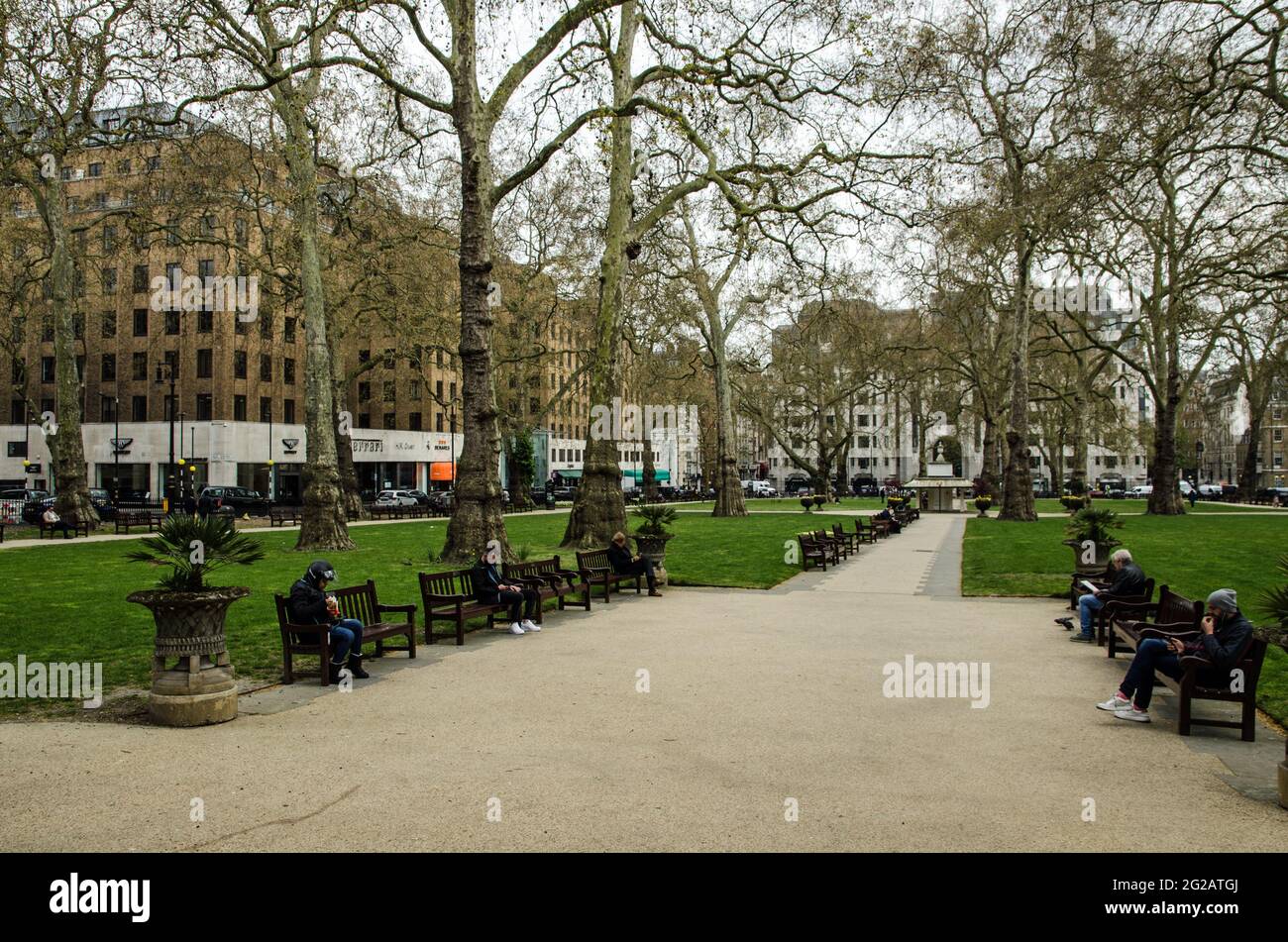 London, Großbritannien - 21. April 2021: Menschen, die an einem kühlen Frühlingsnachmittag die öffentlichen Bänke auf dem berühmten Berkeley Square in Mayfair, London genießen. Stockfoto