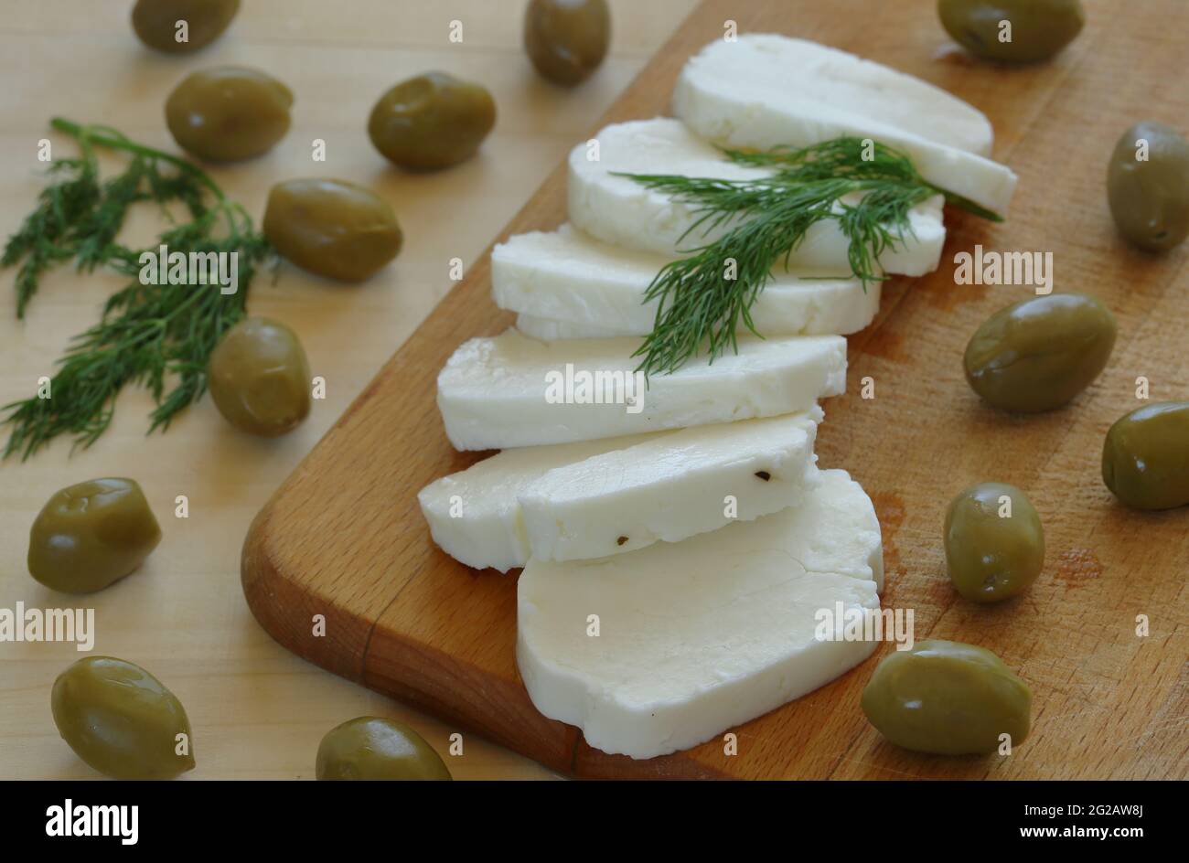 Frische, hausgemachte, traditinale, in Scheiben geschnittene Cyprus-Käse-Halloumi, verziert mit grünen Kräutern auf Holzbrett und Tisch aus nächster Nähe. Stockfoto