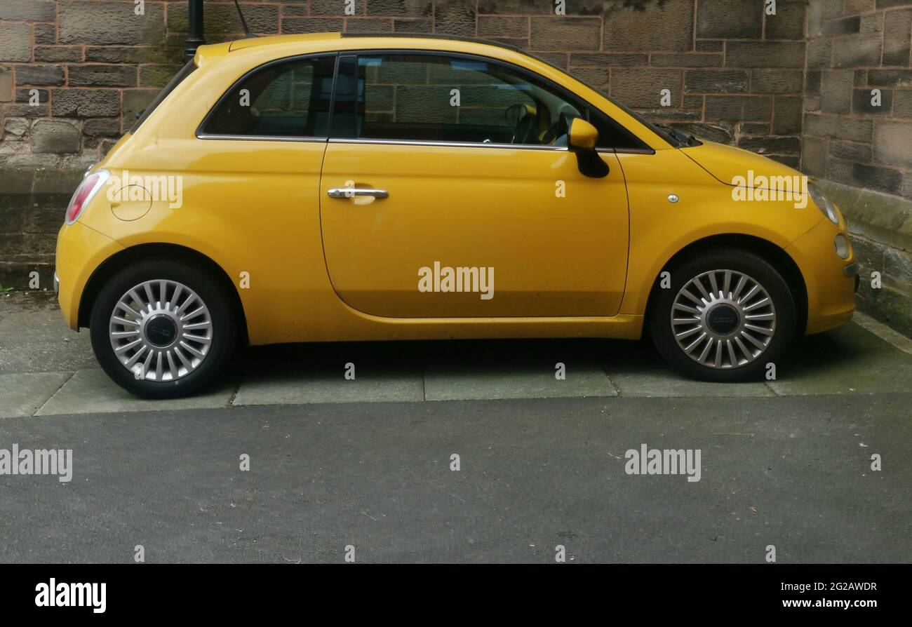 9. Juni 2021 - England, Großbritannien: Dunkelgelber Fiat 500, der von einer alten Mauer eingeparkt wurde Stockfoto