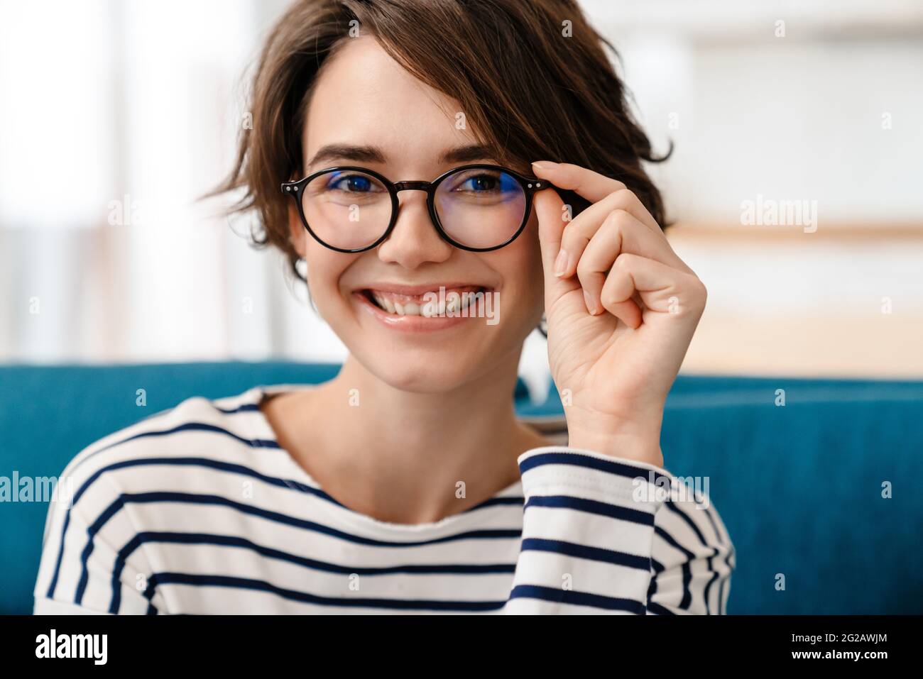 Nahaufnahme einer lächelnden attraktiven jungen Frau mit Brille, die auf einer Couch im Wohnzimmer sitzt Stockfoto