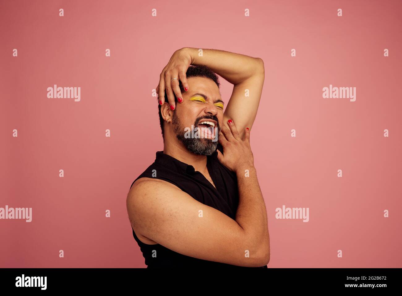Selbstbewusster und ausdrucksstarker Mann auf rosa Hintergrund. Ziehen Sie die Königin in Make-up und lächeln Sie. Stockfoto