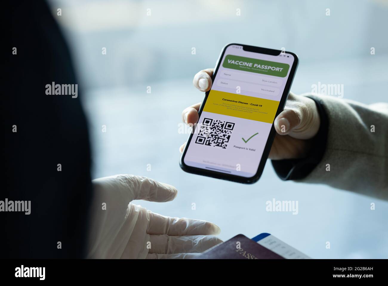 Hand eines Passagiers mit Impfpass am Telefon an den Bodenbegleiter am Flughafen. Der Check-in des Reisenden zeigt den E-Pass für die Immunität an der Flughafenstation Stockfoto