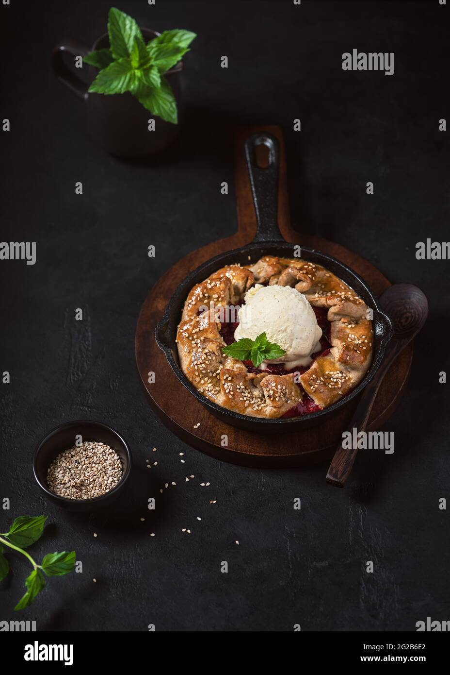 Hausgemachter Galette-Kuchen mit Erdbeeren, Vanilleeis und Sesam im dunklen rustikalen Stil. Stockfoto