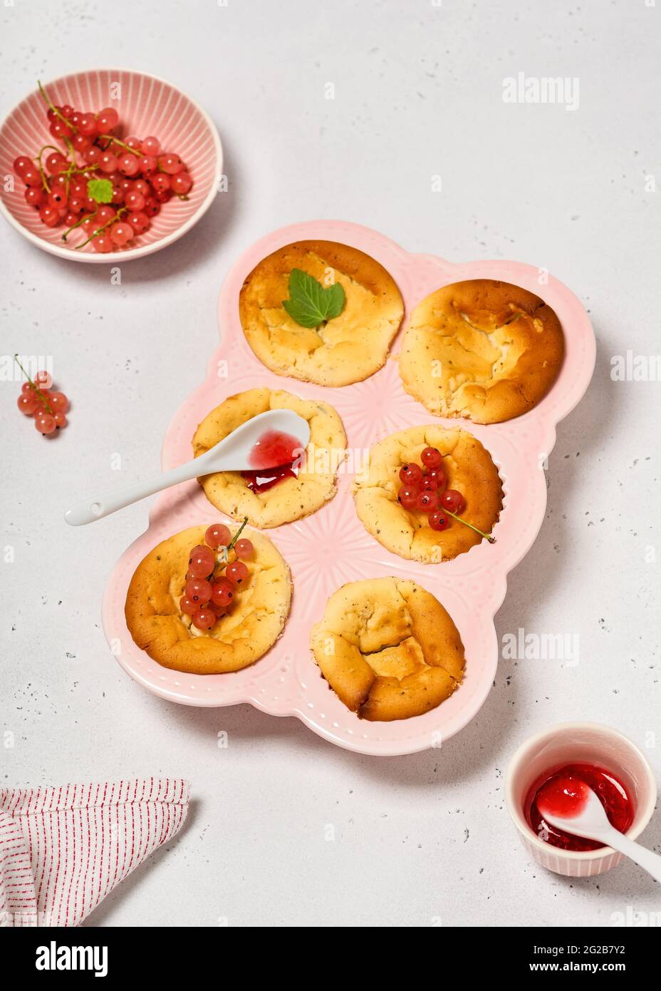 Hausgemachte Mini-Käsekuchen mit rosa Johannisbeer-Fruchtaufstrich und Beeren in einer Keramik-Muffin-Pfanne. Speicherplatz kopieren. Stockfoto