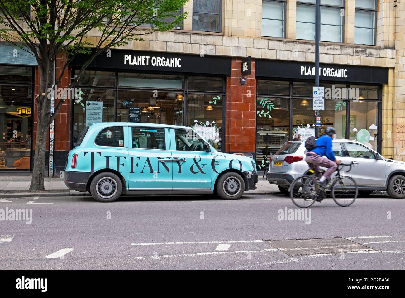 Tiffany & Co-Werbung auf der Seite eines blauen Londoner Taxis, das vor dem Planet Organic Restaurant und Radfahrer in East London geparkt ist E1 UK KATHY DEWITT Stockfoto