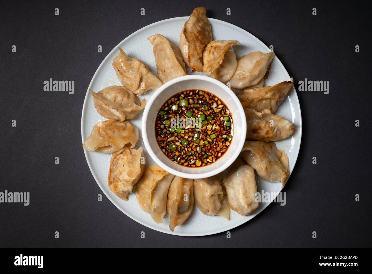 Gebratene Gyoza-Stil Knödel in einem Teller mit würziger Sojasauce auf schwarzem Hintergrund. Asiatische Speisen zum Mitnehmen. Stockfoto