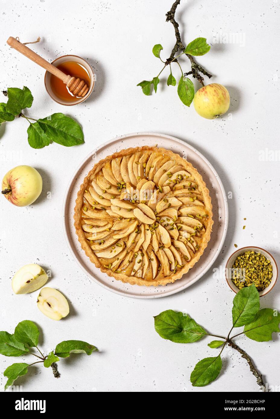 Blick von oben auf frisch gebackene Apfelkuchen-Torte mit Pudding-Füllung und grünen Pistazien auf hellem Stein-Hintergrund. Stockfoto