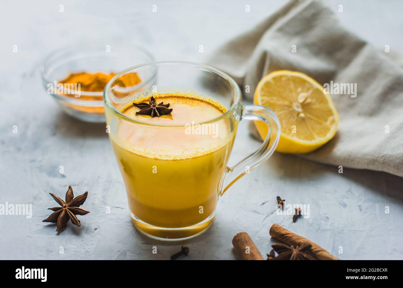 Ein schönes Glas mit goldener Milch, Kurkuma, Gewürzen und Zitrone auf grauem Hintergrund. Gesundes ayurvedisches Getränk. Stärkung des Immunsystems. Antioxi Stockfoto