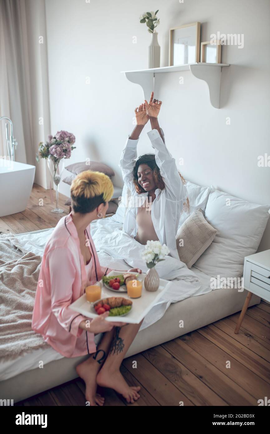 Frau mit Frühstückstablett und Freundin, die aufwachte Stockfoto