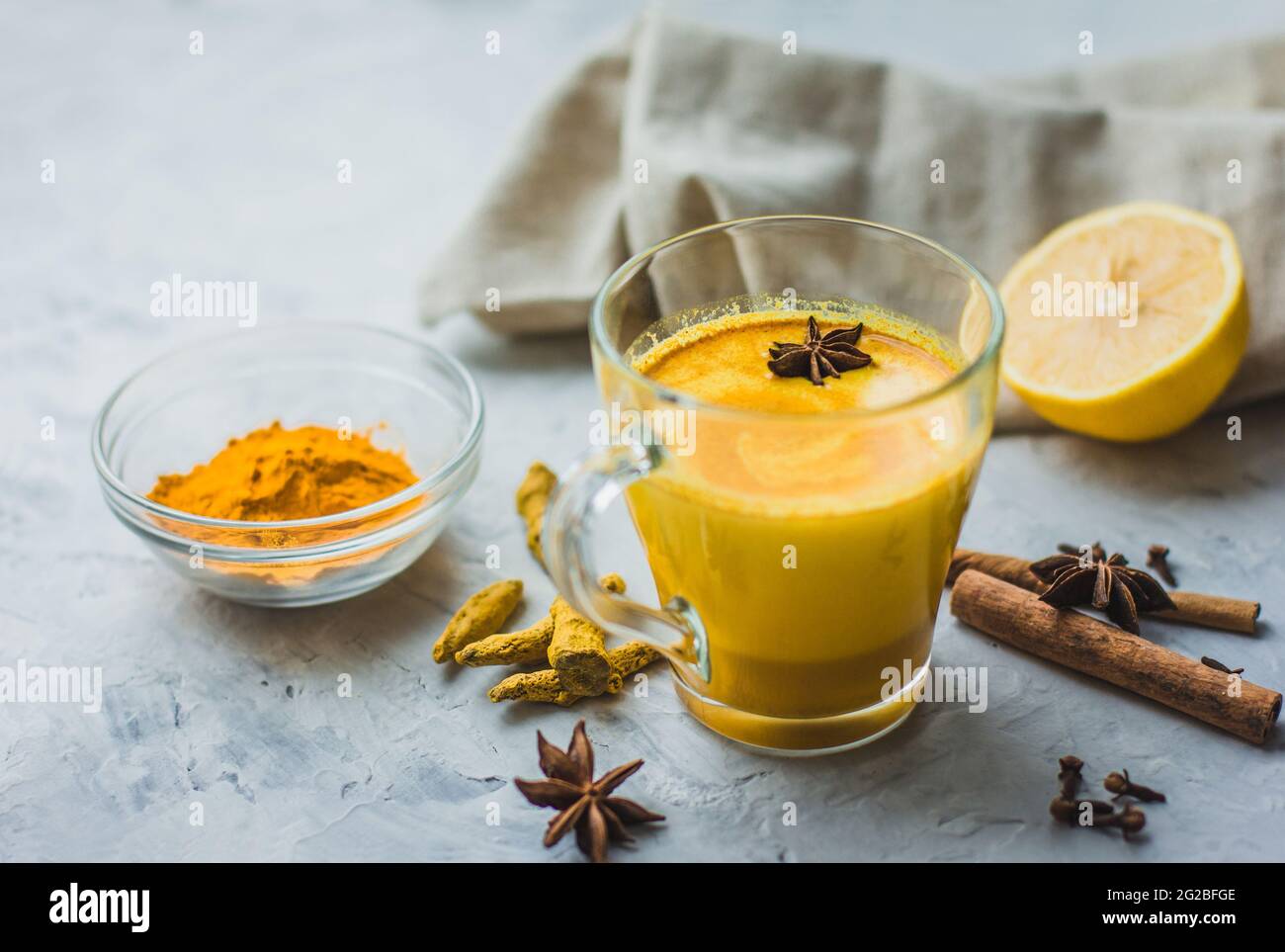 Ein schönes Glas mit goldener Milch, Kurkuma, Gewürzen und Zitrone auf grauem Hintergrund. Gesundes ayurvedisches Getränk. Stärkung des Immunsystems. Antioxi Stockfoto