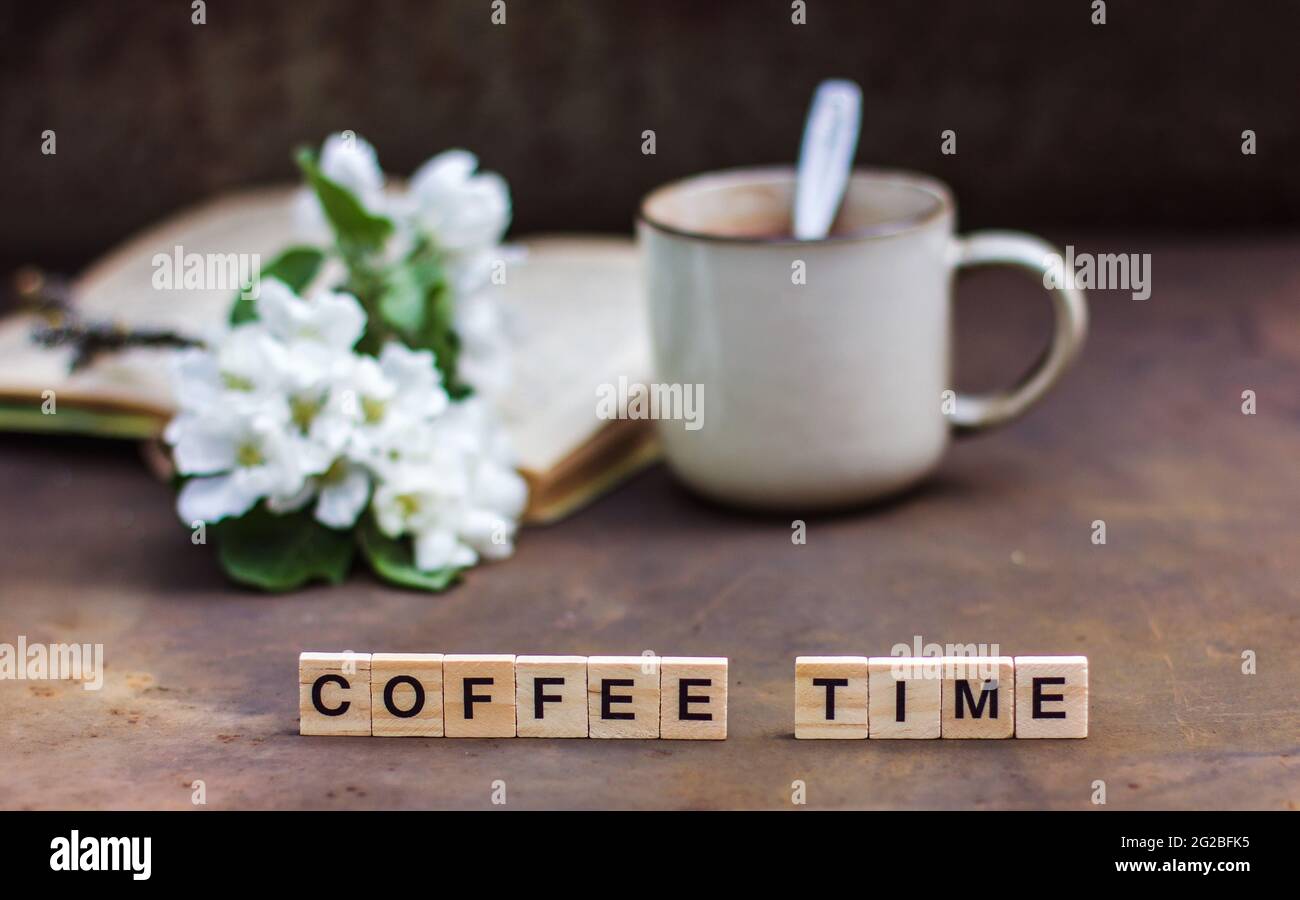 Frühlingsstill-Leben auf dunklem Hintergrund. Die Inschrift 'Coffee Time' EINE Tasse Kaffee, ein Buch, ein blühender Ast eines Apfelbaums. Vintage-Stil phot Stockfoto