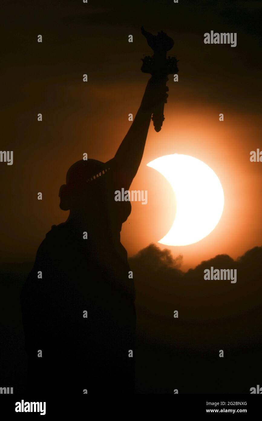 Die teilweise verfinsterte Sonne geht Anfang des 10. Juni 2021 hinter der Freiheitsstatue in New York City, New York, USA, auf. REUTERS/Bjoern Kils/New York Media Boat Stockfoto