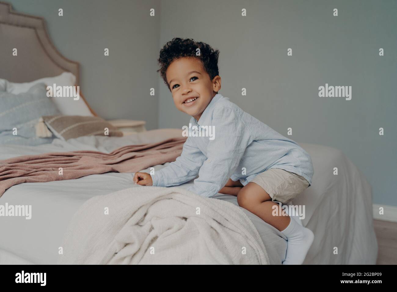 Niedlicher junger afro amerikanischer Junge, der zu Hause auf einem großen Bett spielt Stockfoto