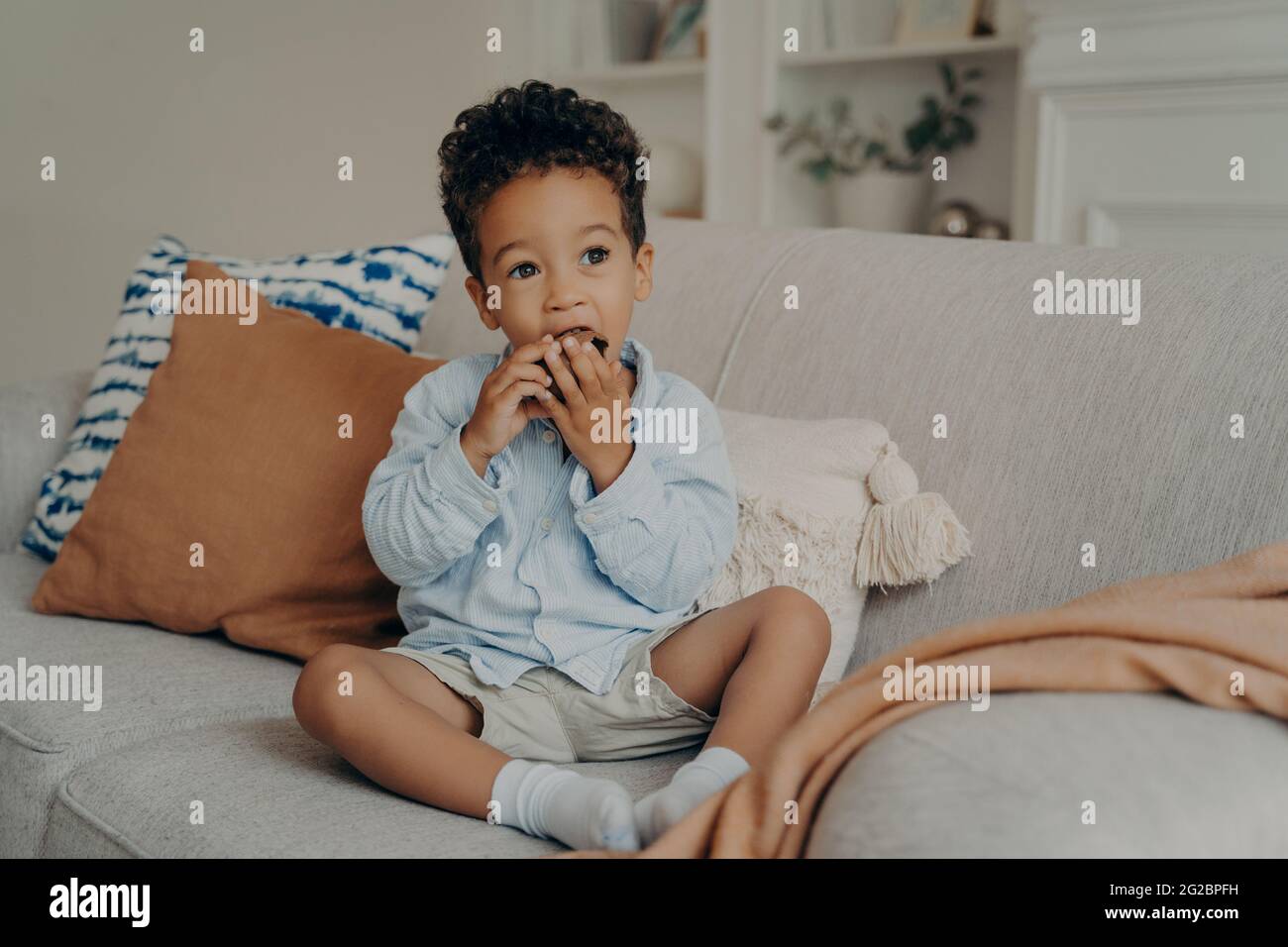 Hungriger netter afro amerikanischer Junge, der Cupcake isst, während er Zeit zu Hause verbringt Stockfoto