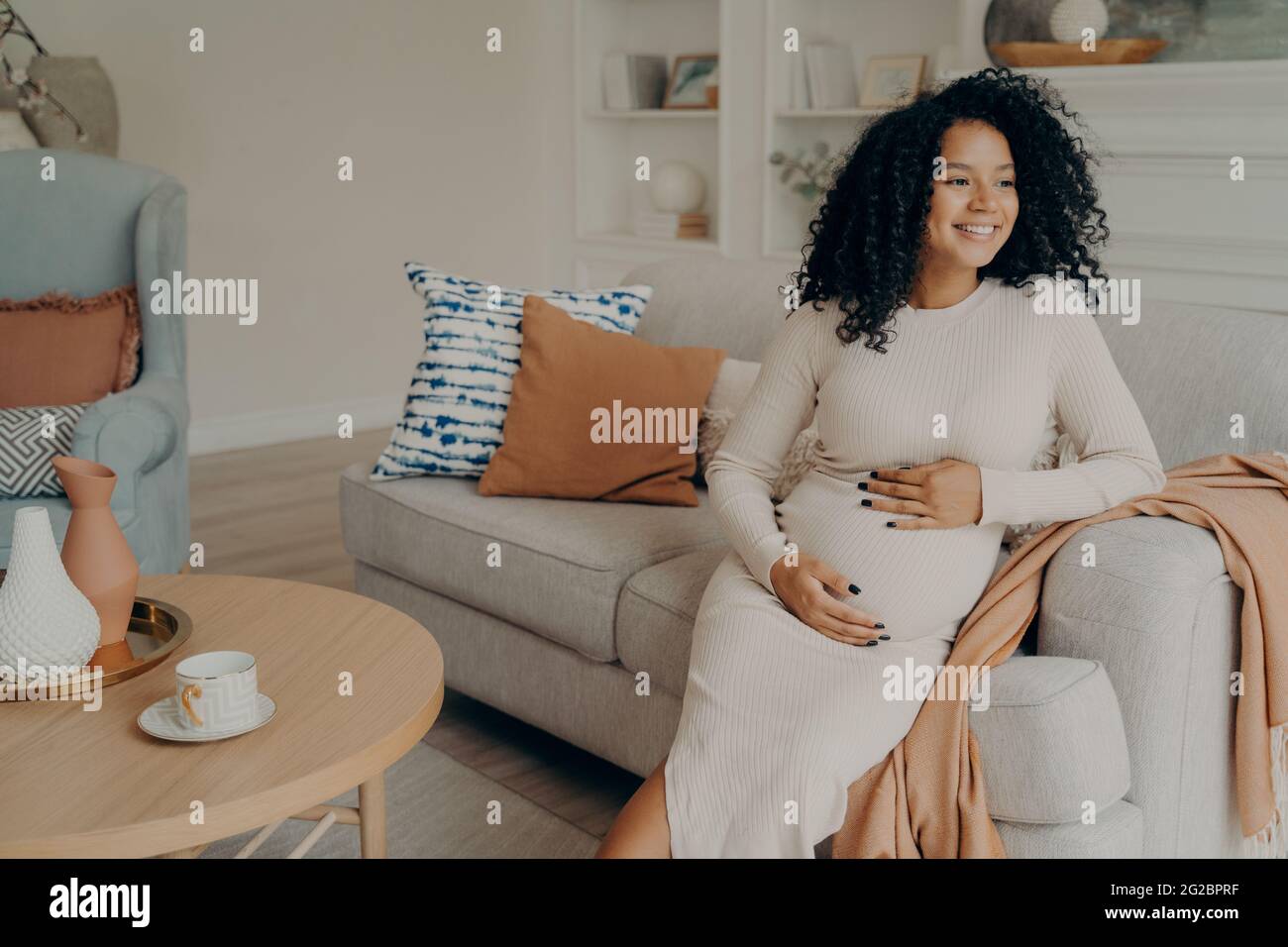 Schwanger afro amerikanische Frau Blick auf das Fenster, während sie auf dem Sofa zu Hause sitzen Stockfoto