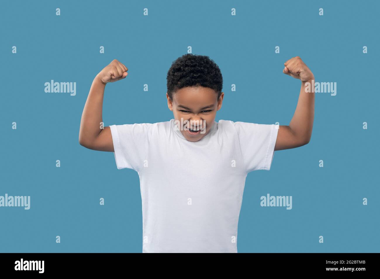Junge zeigt Stärke durch Anspannung der Armmuskeln Stockfoto