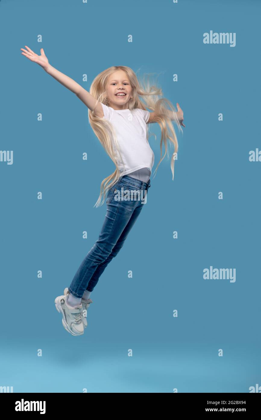 Mädchen springt nach oben mit den Händen zu den Seiten Stockfoto