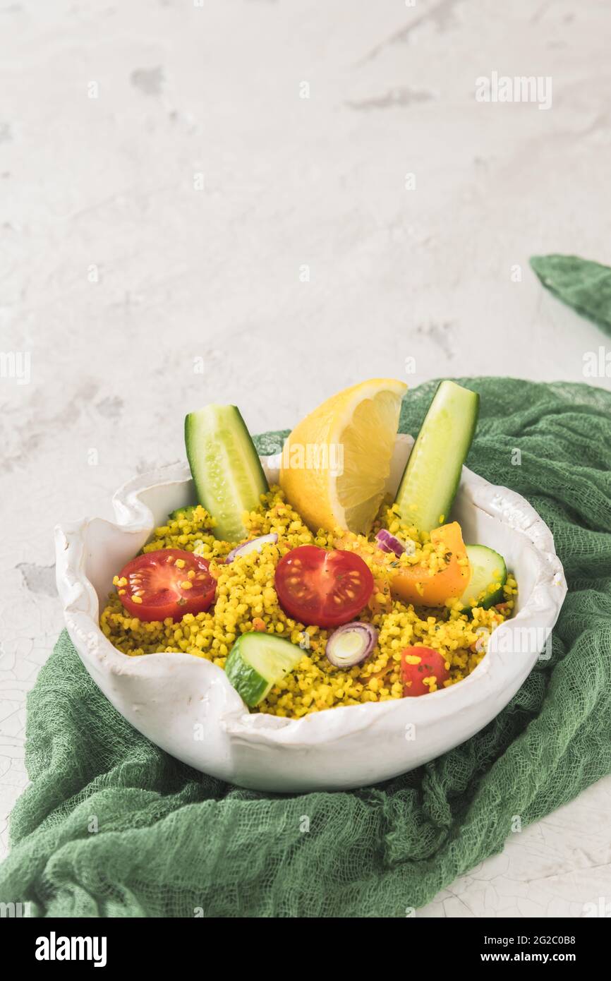 Couscous-Salat mit Gurken, Tomaten und Zwiebeln in einer weißen Schüssel auf weißem Hintergrund, vertikal mit Kopierfläche Stockfoto