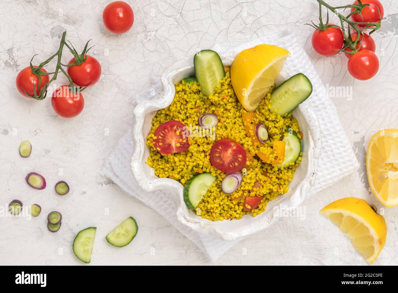 Gesunder Couscous-Salat mit Gurken, Tomaten und Zwiebeln in einer weißen Schüssel auf weißem Hintergrund, Draufsicht Stockfoto