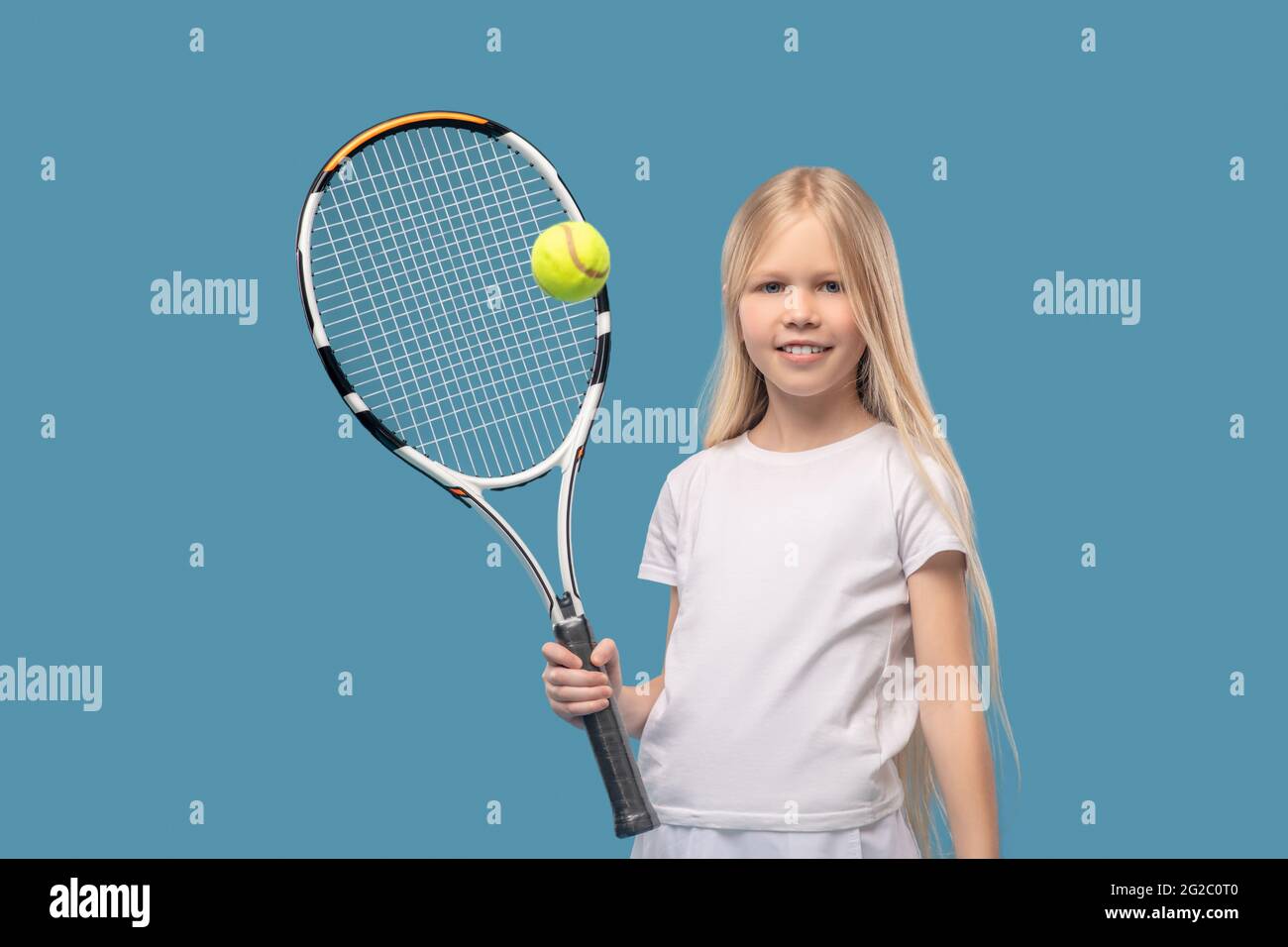 Fröhlicher Teenager-Tennisspieler, der mit Schläger den Ball schlägt Stockfoto