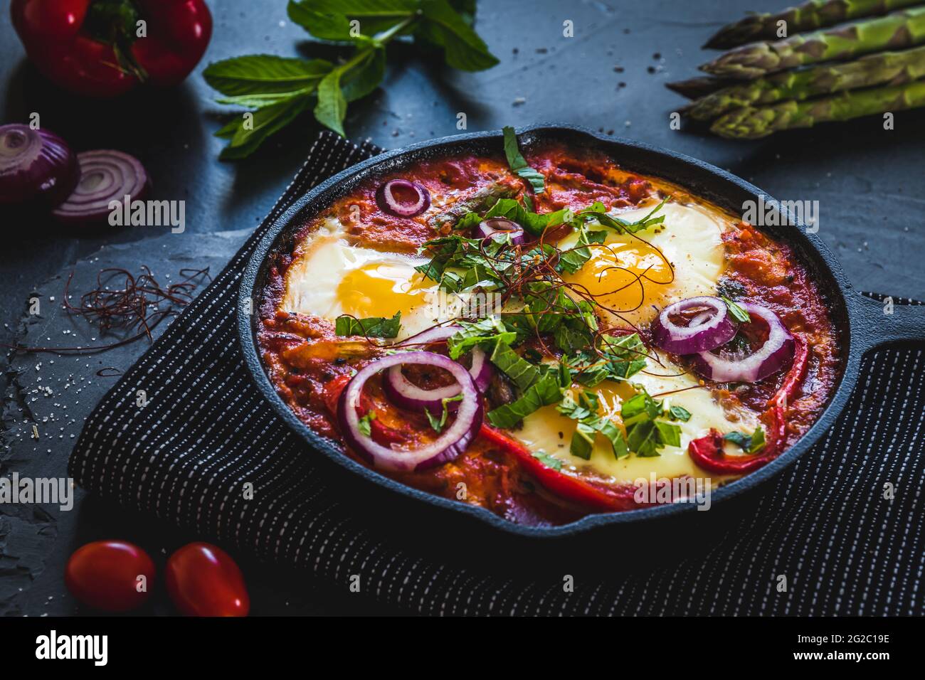 Shakshuka in einer Eisenpfanne. Traditionelles Gericht aus dem Nahen Osten. Spiegeleier mit Tomaten, Paprika, Gemüse und Kräutern, Spiegeleier in sonniger Lage. Stockfoto