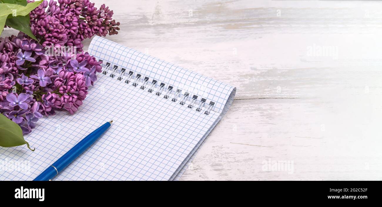 Ein Notizbuch und eine Blume. Ein Notizbuch mit einem Stift und Blumen. Spiralnotizbuch und Stift. Copybook auf einem hölzernen Hintergrund. Stockfoto