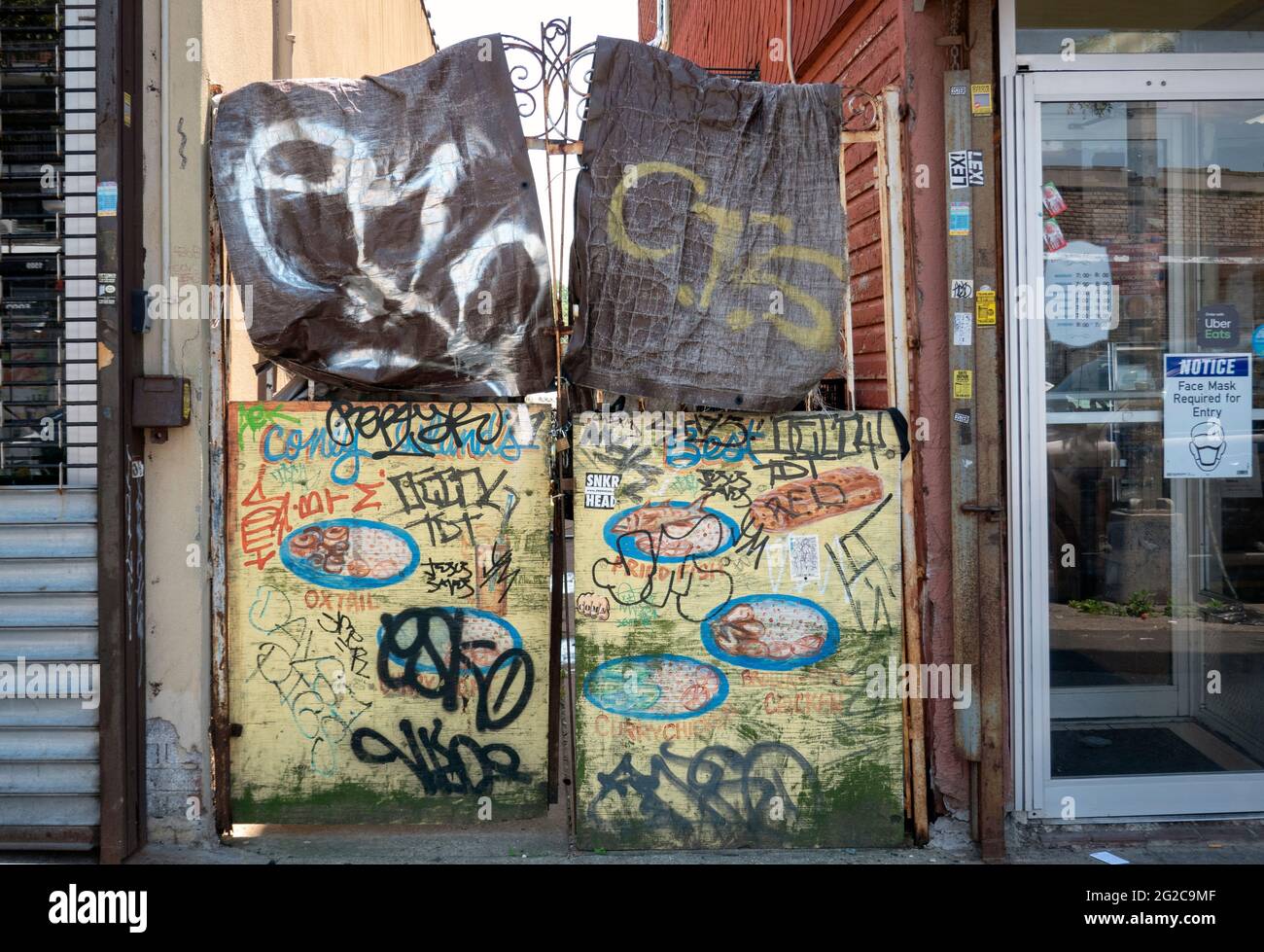 Ein Zaun, der mit Stoff und Holz bedeckt ist und zu einer urbanen Collage aus Graffiti, Aufklebern und Tags wurde. In Coney Island, Brooklyn, New York. Stockfoto
