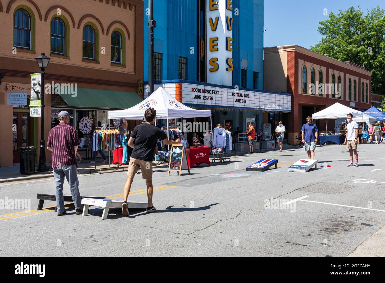 ELKIN, NC, USA-5 JUNE 2021: Vier junge Männer spielen auf einem Stadtstraßenfestival Maisloch oder Maiskolben (werfen Bohnensäcke in Löcher in Bretter). Horizont Stockfoto
