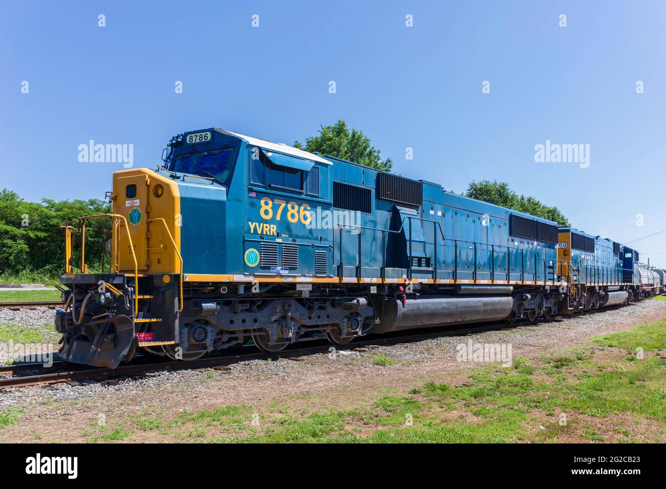 ELKIN, NC, USA-5 JUNE 2021: Eine blau-gelbe Lokomotive und ein Eisenbahnwaggons mit der Bezeichnung „YVRR“ für die Yadkin Valley Railroad. Schwindende Perspektive wetteifern Stockfoto