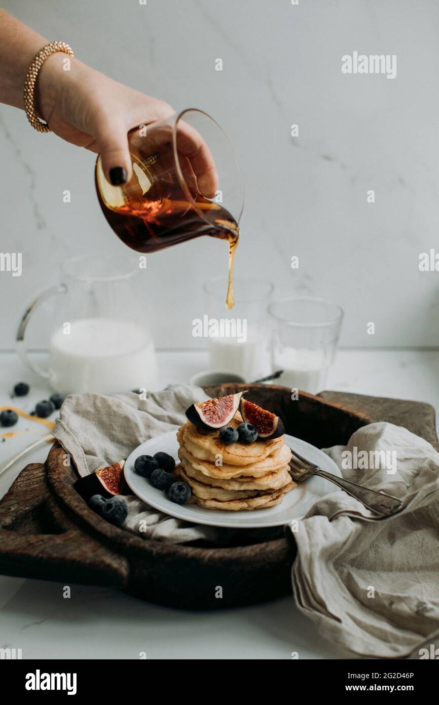 Frau gießt Honig auf Pfannkuchen mit Feigen und Heidelbeeren Stockfoto