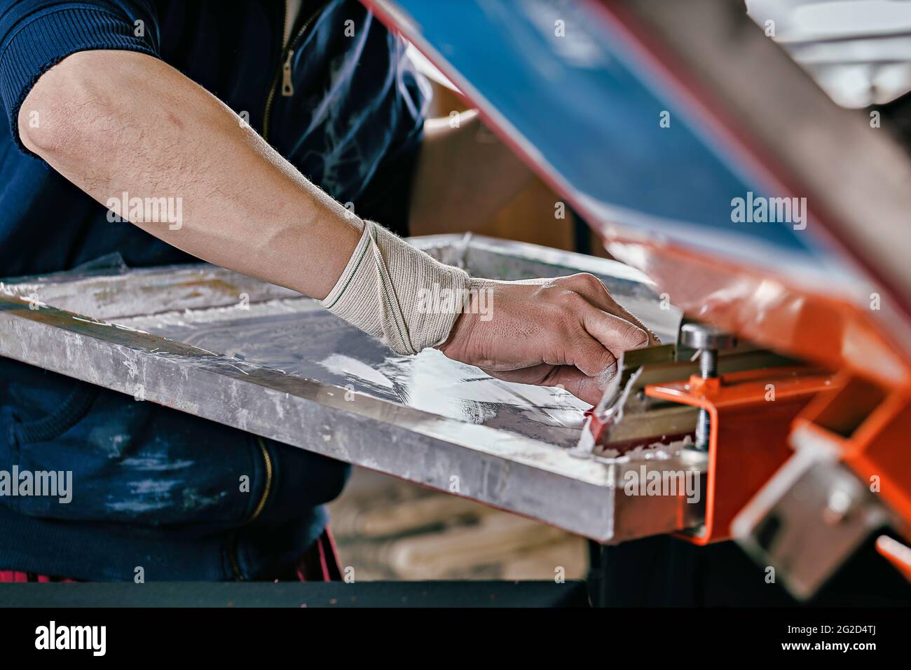 Selektives Fokusfoto der männlichen Hand mit Rakel. Serigraphie-Produktion. Druck von Bildern auf T-Shirts im Siebdruck-Verfahren in einem Designstudio Stockfoto