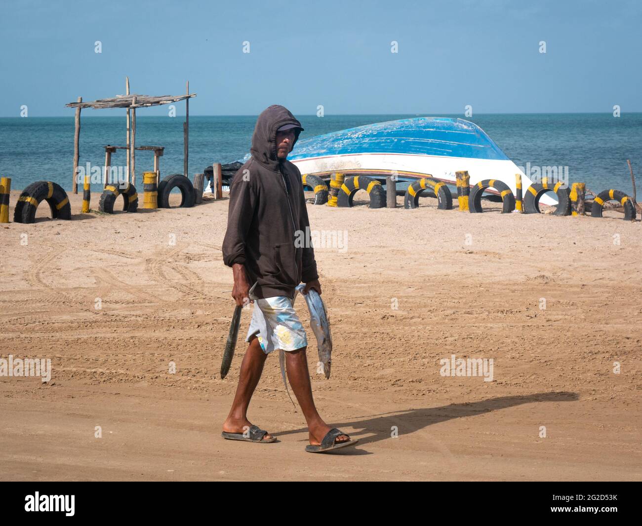 Uribia, La Guajira, Kolumbien - 29 2021. Mai: Lateinischer Mann geht mit Fischen in jeder Hand, nachdem er sie am Strand von Mayapo getötet hat Stockfoto