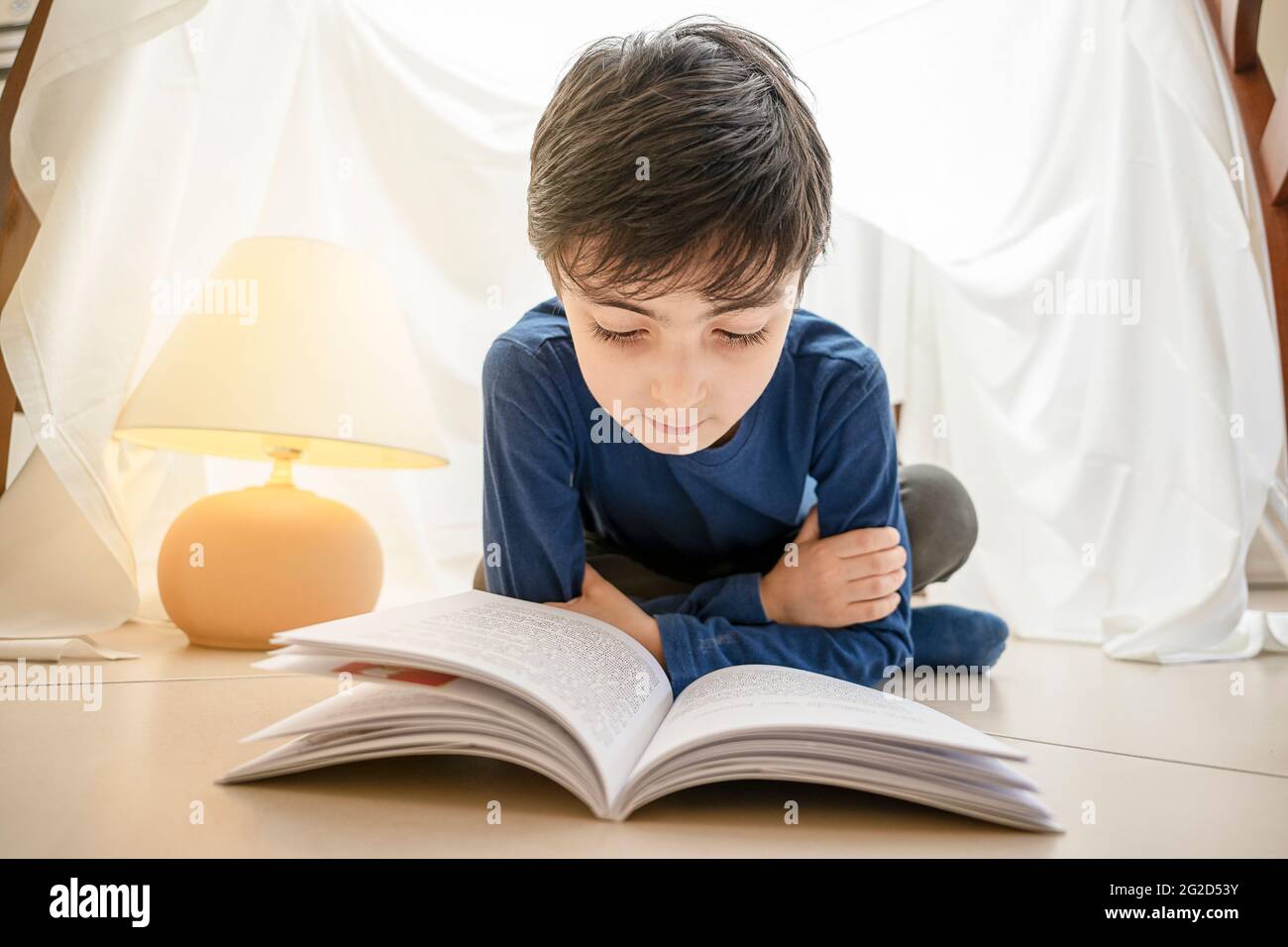 Bezauberndes italienisches kaukasisches Kind, das Buch liest und zu Hause im Zelt liegt Stockfoto