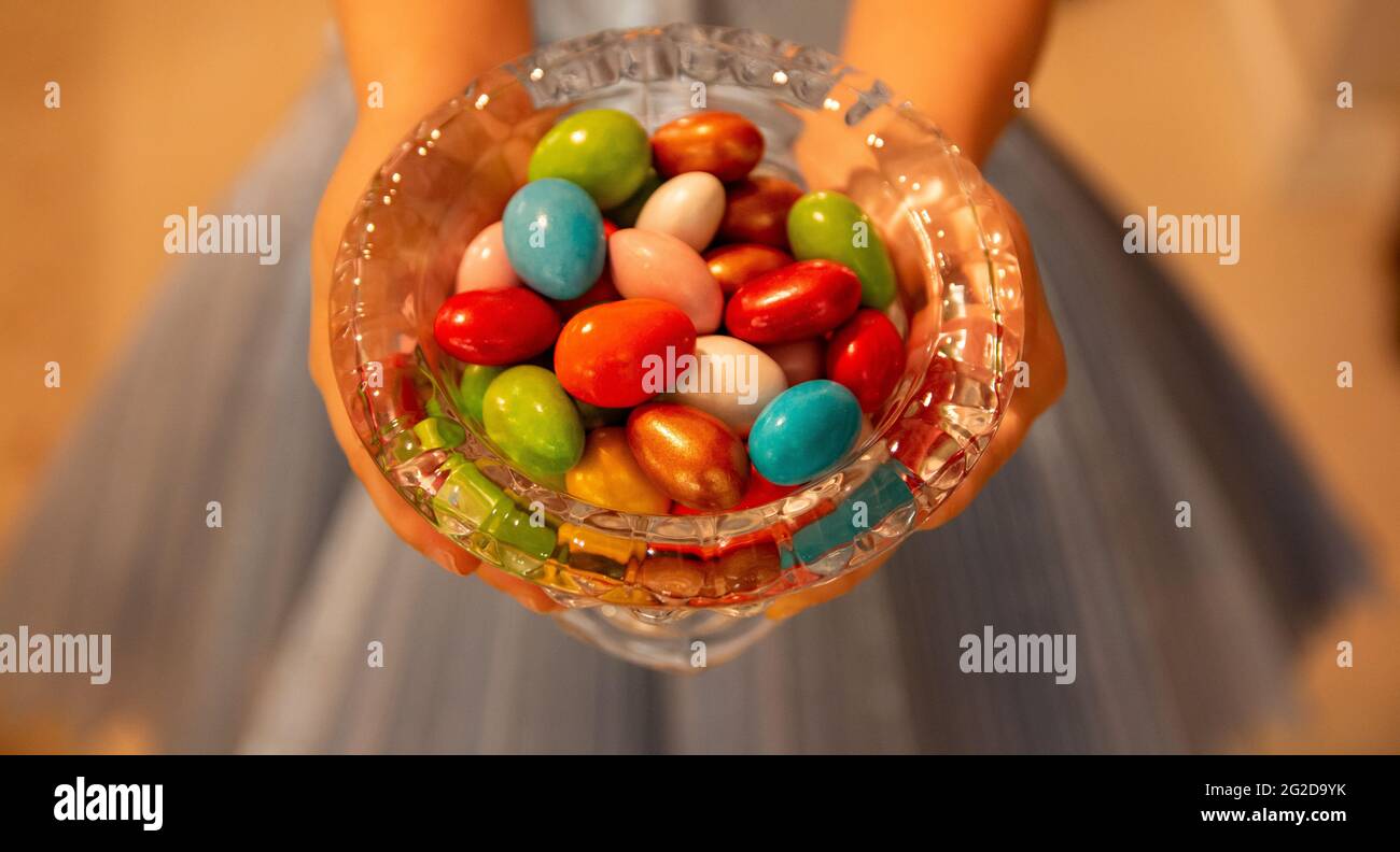 Foto von einem kleinen Mädchen mit blauem Kleid bietet bunte Süßigkeiten für zu Hause begrüßen in das Fest, Süßigkeiten an den Hausgast als Kompliment zu geben Stockfoto