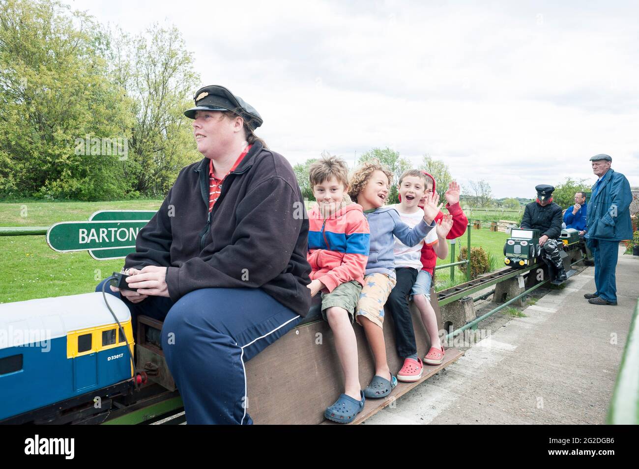 Ein Zugfahrer nimmt Kinder mit in einen lustigen Miniatur-Eisenbahnzug auf Gleisen. Stockfoto